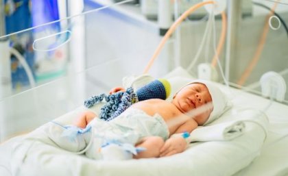 A baby in a hospital bed with an IV tube and bandaged limbs. 